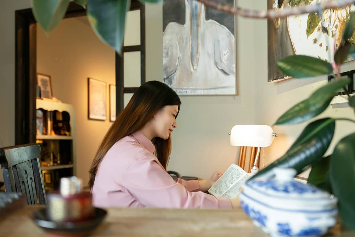 An older woman reading a book in an armchair under a warm, adjustable LED reading lamp angled over her shoulder onto the page