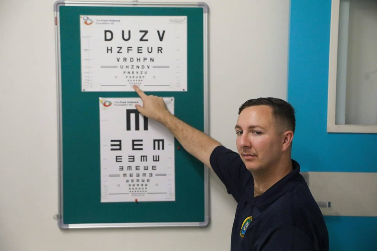 An optician giving an older adult a home eye test in their living room